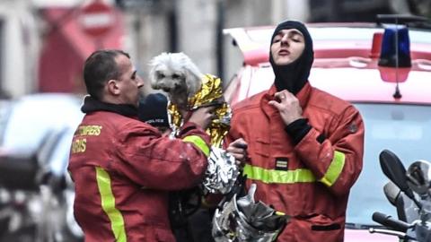 Paris firefighters carry a rescued dog wrapped in a foil blanket near the scene of the fire.