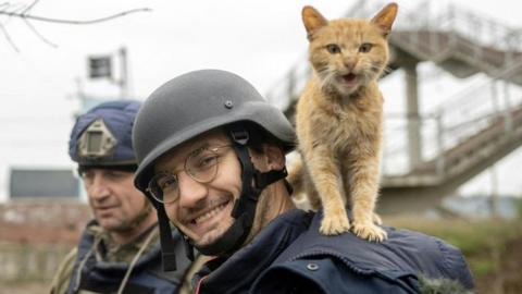 Soldin smiles to the camera as a cat stands on his shoulders during an assignment for AFP in Ukraine