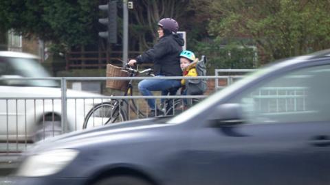 Woman riding bike with child in heavy traffic
