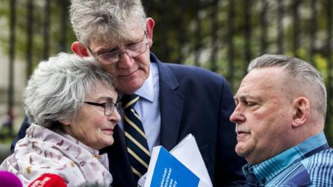 Kate McCausland is embraced by Jon McCourt and accompanied by John Heaney