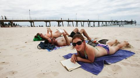 Two women and a man lying on the beach at Glenelg in South Australia.