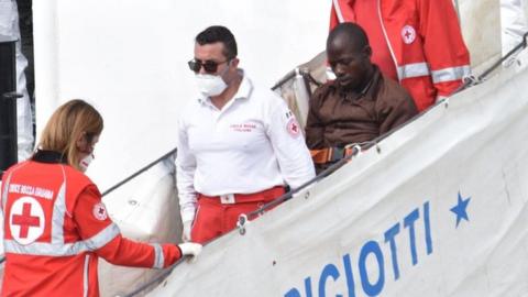 A migrant is helped off the coast guard ship "Diciotti" after arriving at Catania Port, Italy, 13 June 2018