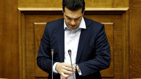 Greek Prime Minister Alexis Tsipras looks at his watch as he delivers a speech during a parliamentary session in Athens on 28 June 2015