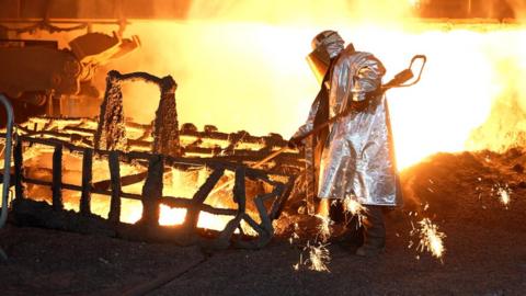 Tata worker in a fireproof suit stoking molten steel