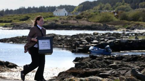 Shona Barton, a member of the Returning Office team from Argyll and Bute Council with ballot boxes as she arrives on the Isle of Gigha