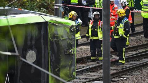 Members of London Fire Brigade look at the overturned tram