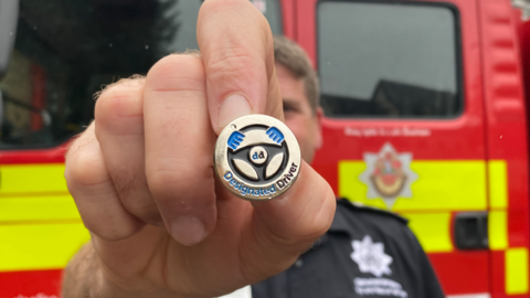 A firefighter holding the designated driver badge in front of a fire engine