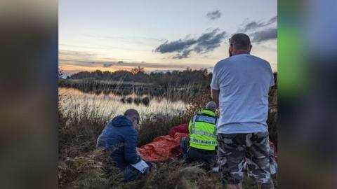 Photo of rescue teams helping the 73-year-old man with the sunset in the background