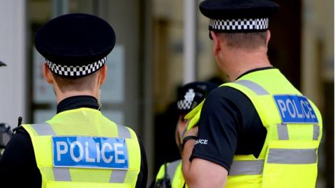 The back of police officers ass they stand on street in high viz yellow vests.