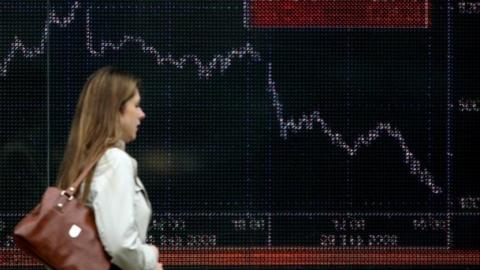 Woman walks past share price graph