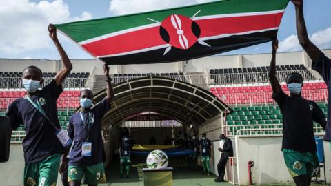 Mascots carry a Kenya flag over a ball at a game