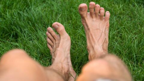 A man's bare legs as he sits on the grass