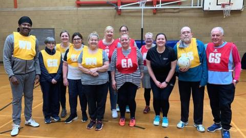 Netball players gathered for photo, wearing red and yellow bibs.