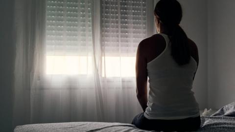 Rear view of a woman sitting on her bed looking out the window