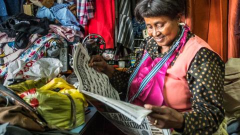 A seamstress reading a newspaper at a Manzini market in Eswatini