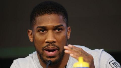 Anthony Joshua talking into a microphone at a news conference for his fight with Robert Helenius