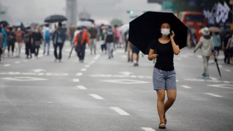 A woman wearing a mask walks past members of conservative civic groups in Seoul, South Korea