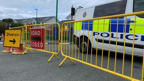 Road closed sign, police van and yellow fencing