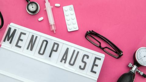 Menopause sign with glasses and a blood pressure gage on a pink background