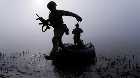 A Ukrainian serviceman jumps out of the boat on the shore of Dnipro river at the frontline near Kherson, Ukraine, Sunday Oct. 15, 2023.