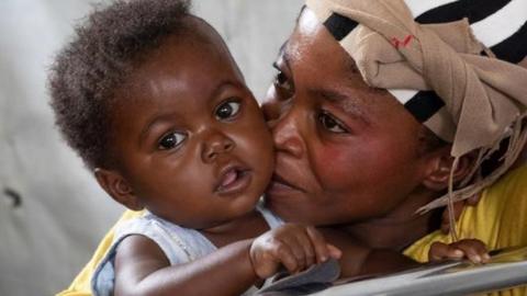 A infant sits in a hospital ward with her mother.