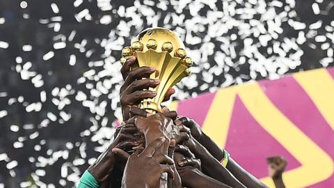 Players lift the Africa Cup of Nations trophy into the air, with ticker tape falling behind