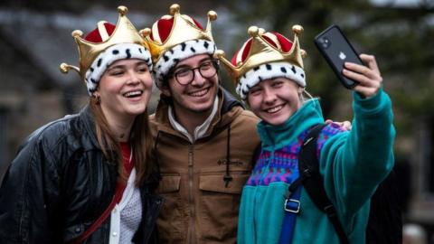 Members of the public, wearing crown-styled hats, pose for a selfie photograph as they attend a 21 gun salute after the Coronation Ceremony for the new King and Queen,