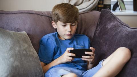 A boy sits on his phone on the sofa
