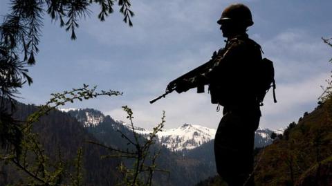n Indian army soldier is silhouetted against the snow capped mountains of Pakistan administered Kashmir as he guards the the Line Of Control on April 20, 2015 i