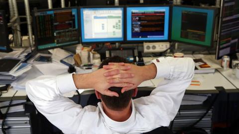 Currency trader leans back and looks at screens