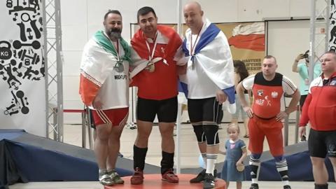 Mostafa Rajai (left) stands on the podium alongside Israeli athlete Maksim Svirsky (right) and another competitor