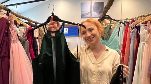 Hannah smiles with dresses in her pre-loved prom shop