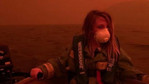 A primary-school aged Australian boy wears a mask and life vest in a in a boat on Mallacoota lake after his family fled into the water to escape the bushfire threatening the town on 31 December 2019