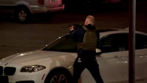 Armed police officer with a gun, behind a car