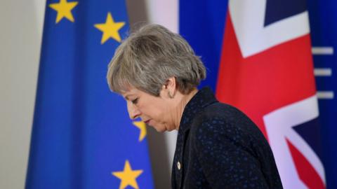 File photo: Theresa May looks down as she walks in front of an EU flag and a UK flag, 22 March 2019