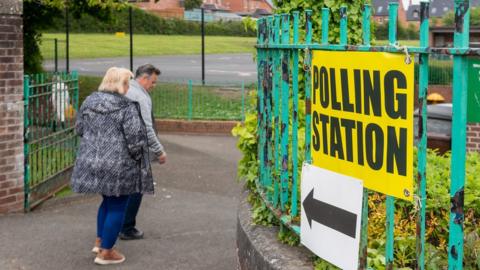 A man and a woman walk through the gates of a Stormont assembly election polling station at a primary school