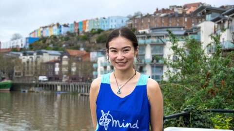 Ella stands in front of Bristol's colourful buildings wearing a Mind running vest