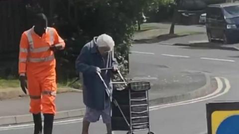 Lorry driver helps a woman across the road