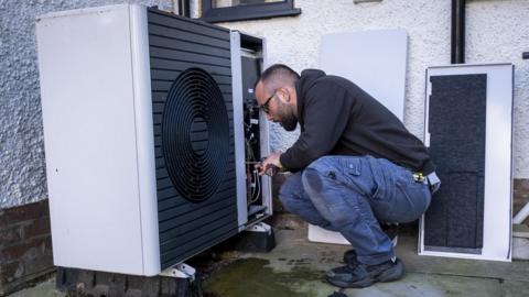 Man bends down next to a heat pump outside a home