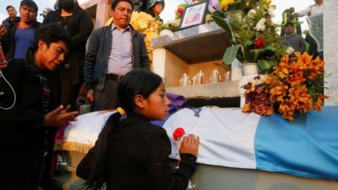A girls holds a flower in front of the coffin with the body of a migrant killed in the Mexican state of Tamaulipas while trying to reach the US in January