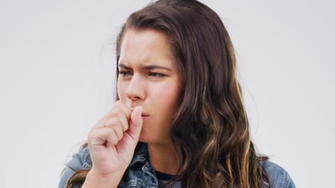 Studio shot of a young woman coughing against a grey background