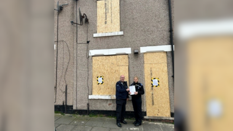 Officers stand outside boarded up home