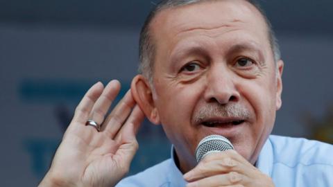President Erdogan cups a hand to his ear in a listening gesture at a rally