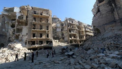 Syrians stand amidst the destruction in the eastern Shaar neighbourhood of the northern Syrian city of Aleppo