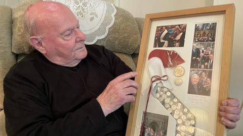 Alec Smith holding a framed Maundy money and photographs from the day