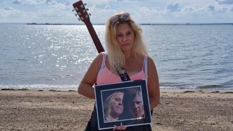 Emma Cain standing on Southend seafront with a picture of her son, Jon Cain