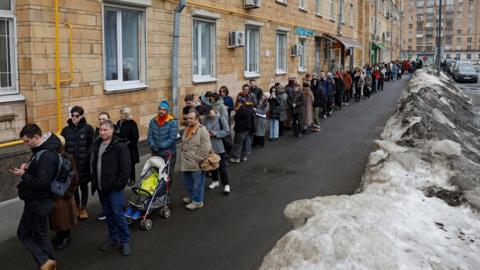 People stand in a line to enter a polling station around noon on the final day of the presidential election in Moscow, Russia