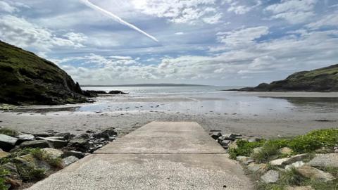 A pathway leading down to a beach with a view out over the sea and a blue cloudy sky.