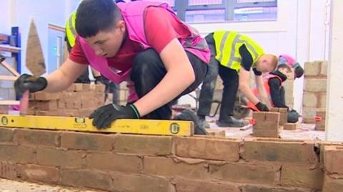 Young man in hi vis vest training how to build a brick wall