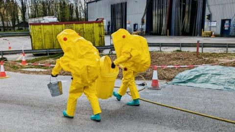 Men in hazard suits getting rid of hazardous waste from bin